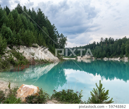 High white bank of the blue pond overgrown with spruces 59748862