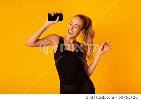 Woman In Wireless Earbuds Holding Smartphone And Dancing, Studio Shot Woman In Wireless Earbuds Holding Smartphone And Dancing, Studio Shot 59753420