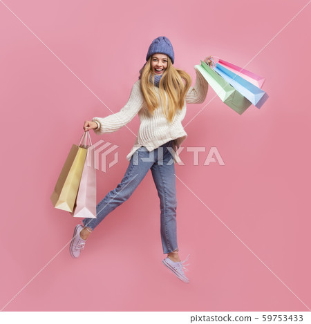 Cheerful shopaholic girl with purchases jumping cause of happiness Cheerful shopaholic girl with purchases jumping cause of happiness 59753433