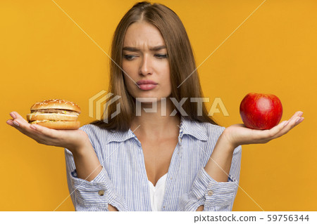 Lady Holding Burger And Apple Standing Choosing Food, Studio Shot 59756344