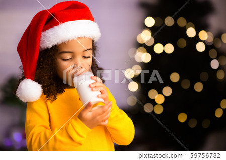 Little african girl drinking warm milk near Christmas tree Little african girl drinking warm milk near Christmas tree 59756782