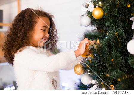 Cute african american girl decorating Christmas tree Cute african american girl decorating Christmas tree 59757373