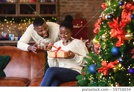 Excited black wife unwrapping christmas present from her husband Excited black wife unwrapping christmas present from her husband 59758034