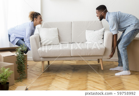 Cheerful Afro Spouses Placing Couch Furnishing Empty Room In New House 59758992