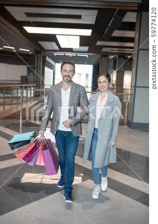 Couple smiling while leaving shopping center after successful shopping Couple smiling while leaving shopping center after successful shopping 59774120