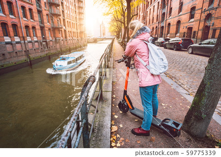 Adult woman tourist with backpack on e-scooter enjoying most famous historic Speicherstadt warehouse 59775339
