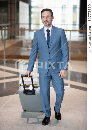 Serious successful businessman walking with luggage in the hotel 59775459