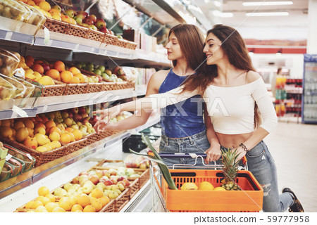 Two women who choose bioproducts produce in a supermarket with fruit from the shopping list. 59777958
