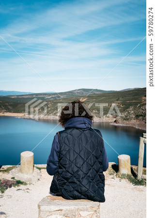 Rear view of woman sitting gazing at lake 59780274