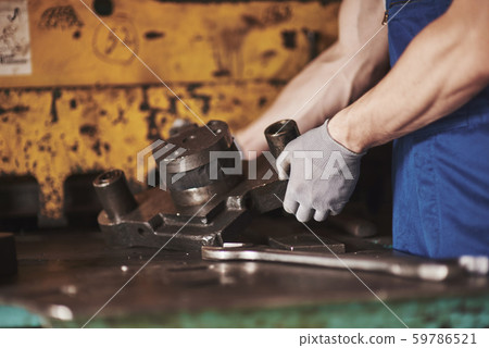 Strong hands hold the steel part. In the old factory. Strong hands hold the steel part. In the old factory. 59786521