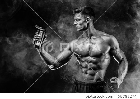 Muscular man with protein drink in shaker over dark smoke background Muscular man with protein drink in shaker over dark smoke background 59789274