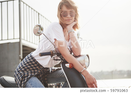 Portrait of a beautiful girl hipster sitting on a black retro scooter, smiling posing and enjoy the 59791063