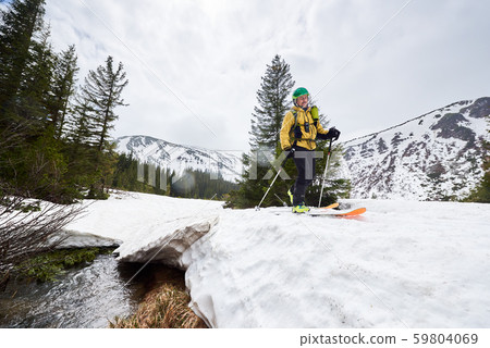 Backcountry skiing. Happy man skier in ski touring and sliding on snow-covered road over flowing 59804069