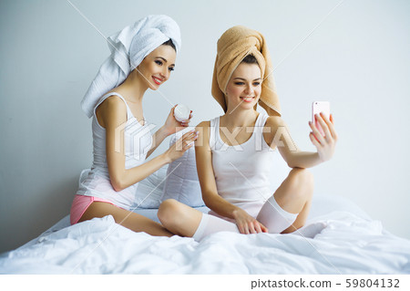 Two cheerful sisters with perfect skin siting on bed after bath Two cheerful sisters with perfect skin siting on bed after bath 59804132