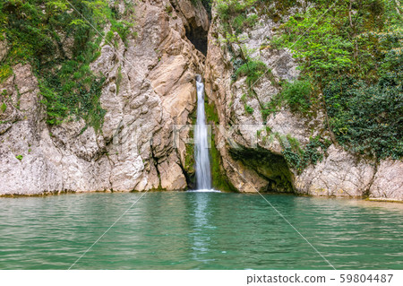 A high waterfall falls from a cliff into a clear lake A high waterfall falls from a cliff into a clear lake 59804487