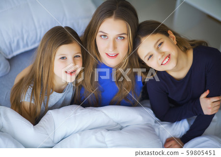 Happy family playing at home. Mother and toddler daughters relaxing and having fun in bed in cozy 59805451