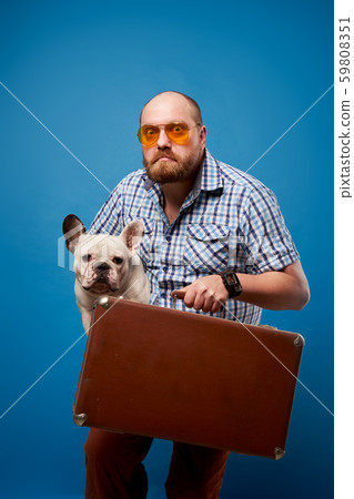 Bearded man in glasses with bulldog and luggage on empty blue background 59808351