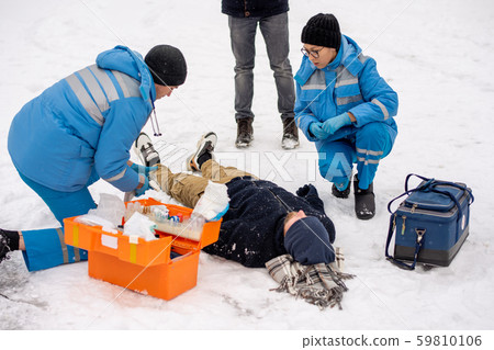 Group of young paramedics in winter uniform helping sick unconscious man 59810106