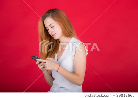 Young, beautiful red-haired woman isolated on a red background, looks at the phone screen. 59812663