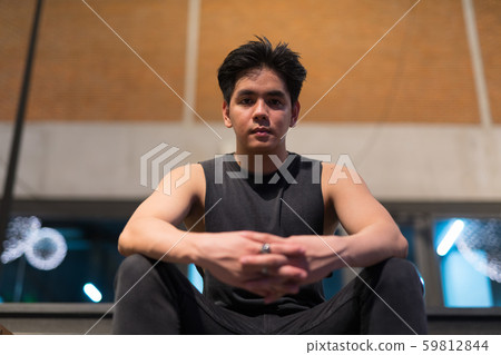 Young handsome Asian man sitting in the city outdoors at night Young handsome Asian man sitting in the city outdoors at night 59812844