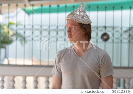 Young man with tin foil hat thinking as conspiracy theory concept outdoors Young man with tin foil hat thinking as conspiracy theory concept outdoors 59812889