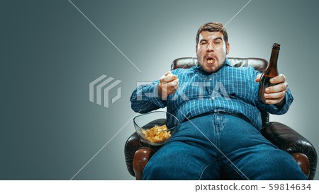 Fat man sitting in a brown armchair, emotional watching TV 59814634