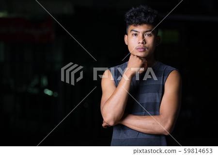 Young Asian man thinking and looking at camera at night outdoors Young Asian man thinking and looking at camera at night outdoors 59814653