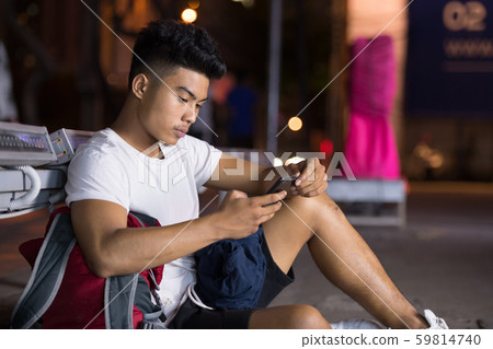 Young Asian man using phone in the city streets at night Young Asian man using phone in the city streets at night 59814740