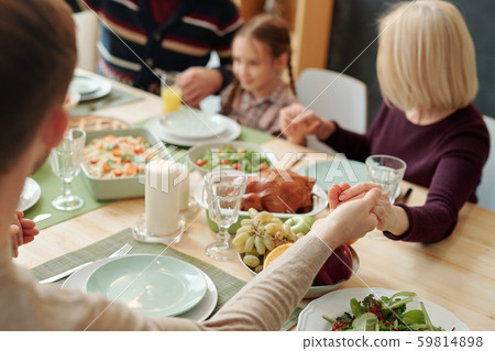 Hands of family held by each other over served festive table during pray Hands of family held by each other over served festive table during pray 59814898
