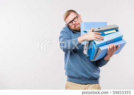 Busy young bearded office manager with smartphone by ear and stack of folders 59815355