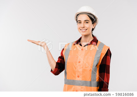 Pretty young smiling female builder in hardhat and workwear presenting something 59816086