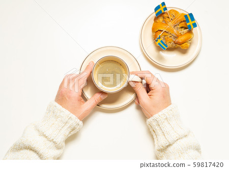 Swedish cinnamon bun (kanelbull) and coffee cup in hands on the white wooden table. Swedish flags. Coffee break (fika) concept. 59817420