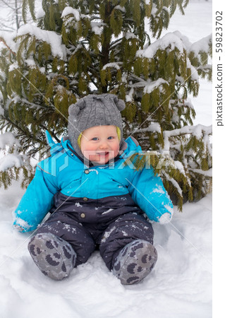 A little boy sitting in the snow under the tree in 59823702