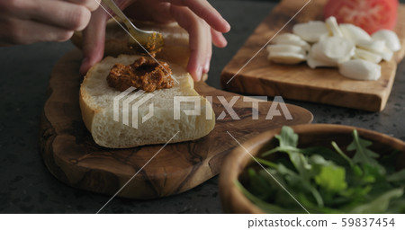 man spread red pesto on ciabatta slice on olive board man spread red pesto on ciabatta slice on olive board 59837454