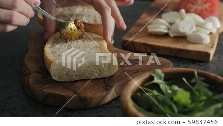 man spread red pesto on ciabatta slice on olive board man spread red pesto on ciabatta slice on olive board 59837456