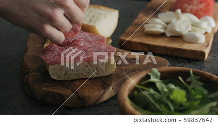 man put salami on ciabatta slice on olive board man put salami on ciabatta slice on olive board 59837642