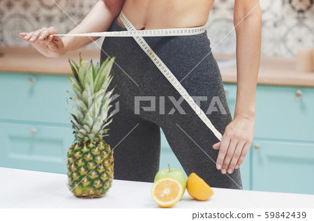Portrait of a woman measuring her slim body on a kitchen background. Fitness and healthy lifestyle 59842439