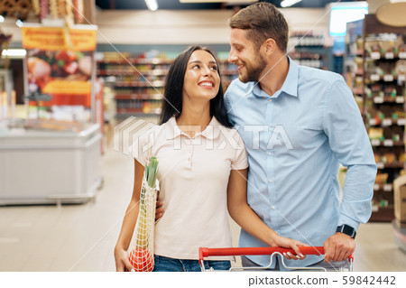 Daily Shopping. Couple in the supermarket walking with cart together looking at each other laughing 59842442