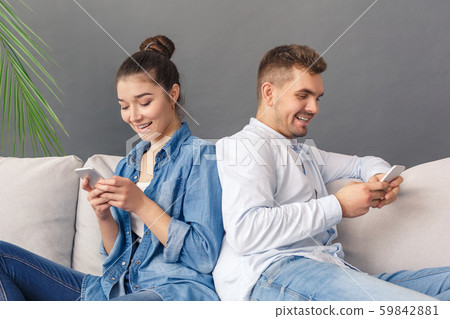 Modern Relatonship. Young couple sitting on sofa studio isolated on grey chatting online on Modern Relatonship. Young couple sitting on sofa studio isolated on grey chatting online on 59842881