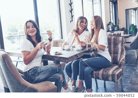 The three best girlfriends gathered to drink coffee and gossip. Girls having fun and laughing 59844852