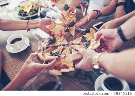 Dinner time. Close-up of tasty pizza on the table, with a lot of hands that take a piece Dinner time. Close-up of tasty pizza on the table, with a lot of hands that take a piece 59845116