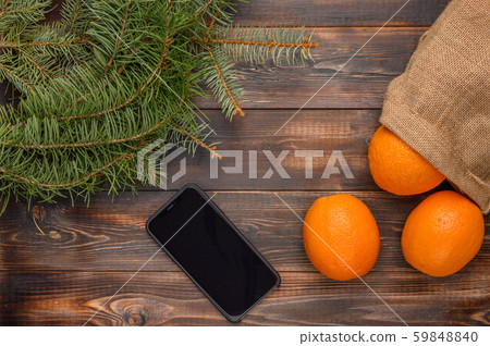 Oranges in a linen bag on a wooden background. Near fir branches and black smartphone. Christmas Oranges in a linen bag on a wooden background. Near fir branches and black smartphone. Christmas 59848840