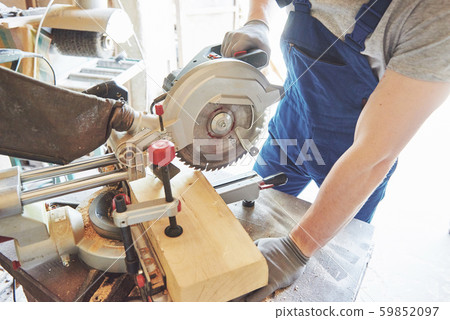 Master in a work suit using a grinder on a sawmill. Master in a work suit using a grinder on a sawmill. 59852097