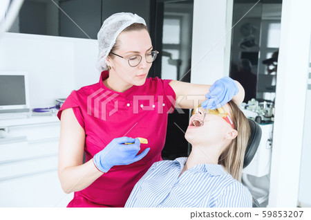 In the dentist's office. A female dentist in glasses is preparing to make a cast of the jaw of a 59853207