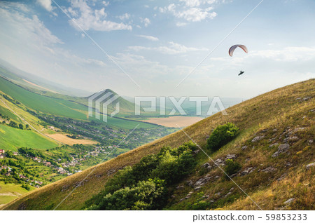 A paraglider flies in the sky in a cocoon suit on a paraglider over the Caucasian countryside with A paraglider flies in the sky in a cocoon suit on a paraglider over the Caucasian countryside with 59853233