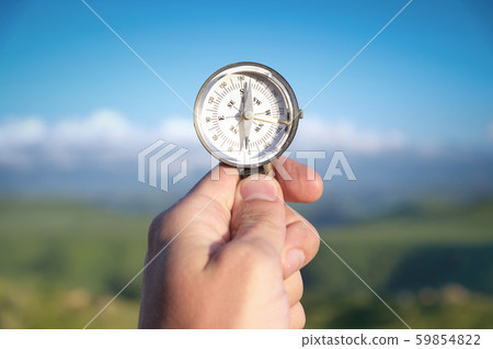 Man searching direction with a compass in his hand in the summer mountains point of view. Direction Man searching direction with a compass in his hand in the summer mountains point of view. Direction 59854822