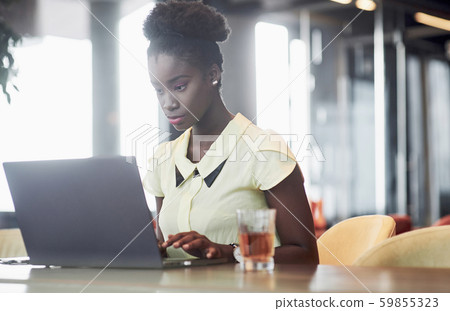 A young African American girl with dark curly hair pondering a laptop in a cafe A young African American girl with dark curly hair pondering a laptop in a cafe 59855323