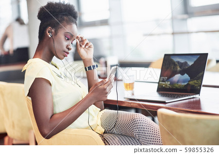A young African American girl with dark curly hair pondering a laptop in a cafe A young African American girl with dark curly hair pondering a laptop in a cafe 59855326