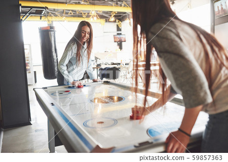 Two beautiful twin girls play air hockey in the game roomand have fun Two beautiful twin girls play air hockey in the game roomand have fun 59857363