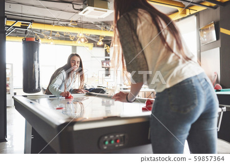 Two beautiful twin girls play air hockey in the game roomand have fun Two beautiful twin girls play air hockey in the game roomand have fun 59857364